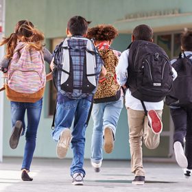 Primary school kids running with their backpacks towards the school doors